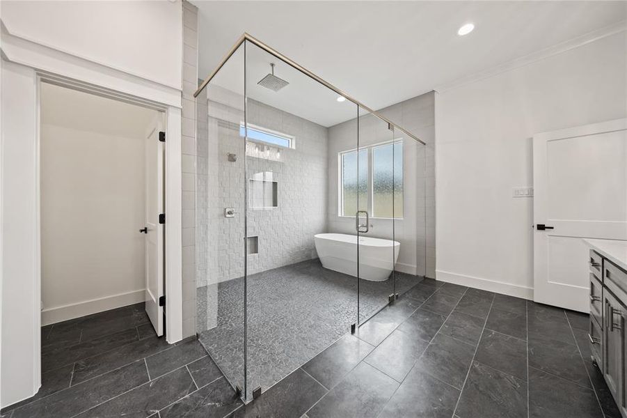 Bathroom featuring a frameless glass shower enclosure, a freestanding soaking tub, dark rectangular floor tiles, light tiled shower walls with niche shelving, and a window providing natural illumination