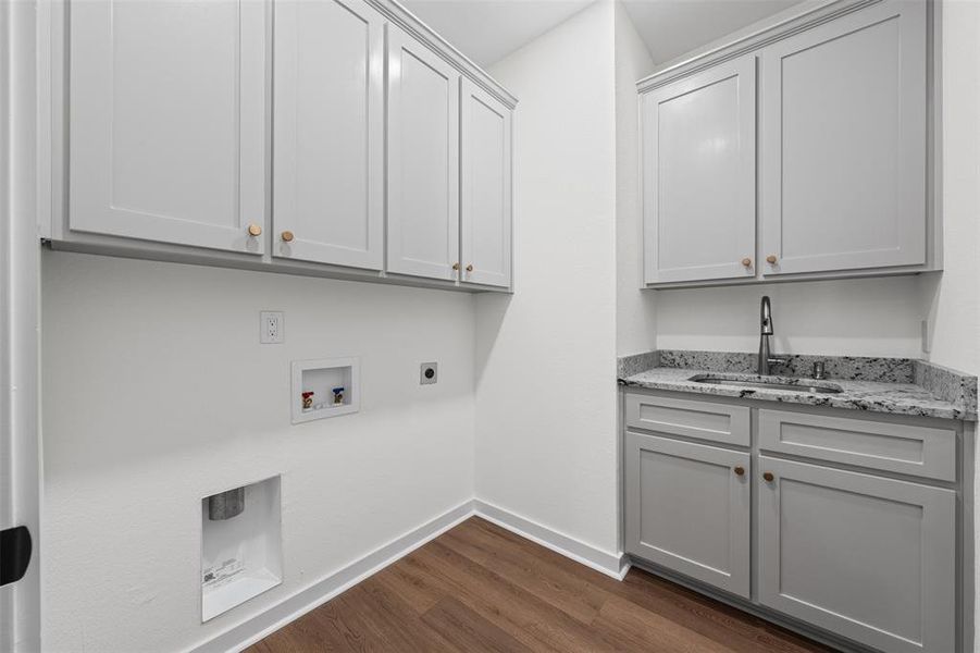 Well-appointed laundry room with grey cabinetry, granite countertops, a stainless steel sink, and wood-look flooring