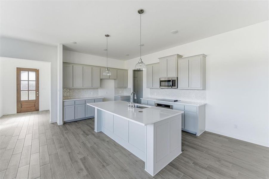 Kitchen with decorative backsplash, a center island with sink, gray cabinetry, light wood-style flooring, and stainless steel appliances