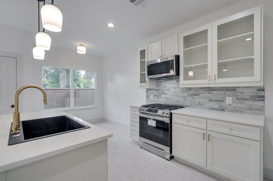 Kitchen with sink, decorative light fixtures, appliances with stainless steel finishes, decorative backsplash, and white cabinets