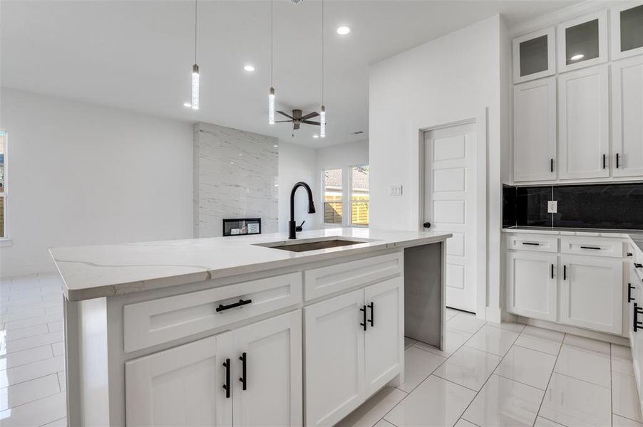 Kitchen featuring white cabinets, pendant lighting, light stone countertops, an island with sink, and tasteful backsplash