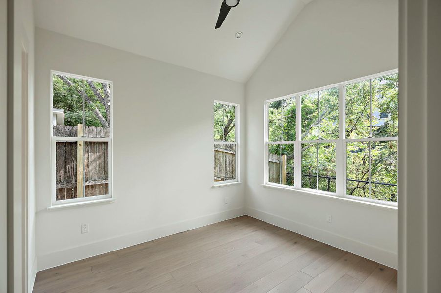 Spare room featuring plenty of natural light, a ceiling fan, baseboards, light wood-type flooring, and high vaulted ceiling