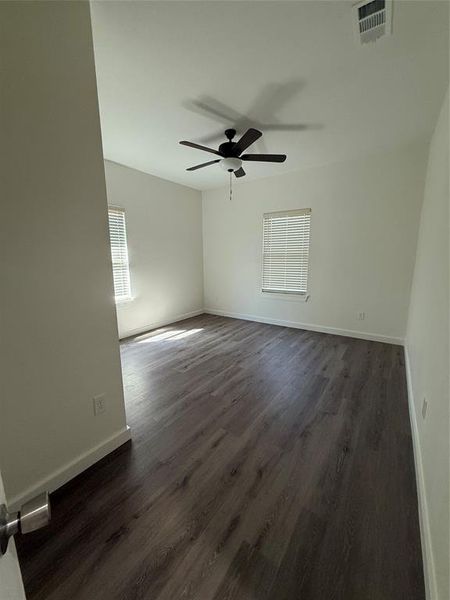 Unfurnished room featuring dark wood-type flooring, a ceiling fan, visible vents, and baseboards