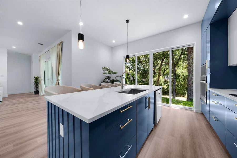 Kitchen with blue cabinetry, light wood-style flooring, a center island with sink, pendant lighting, and light stone countertops Kitchen with blue cabinetry, light wood-style flooring, a center island with sink, pendant lighting, and light stone countertops