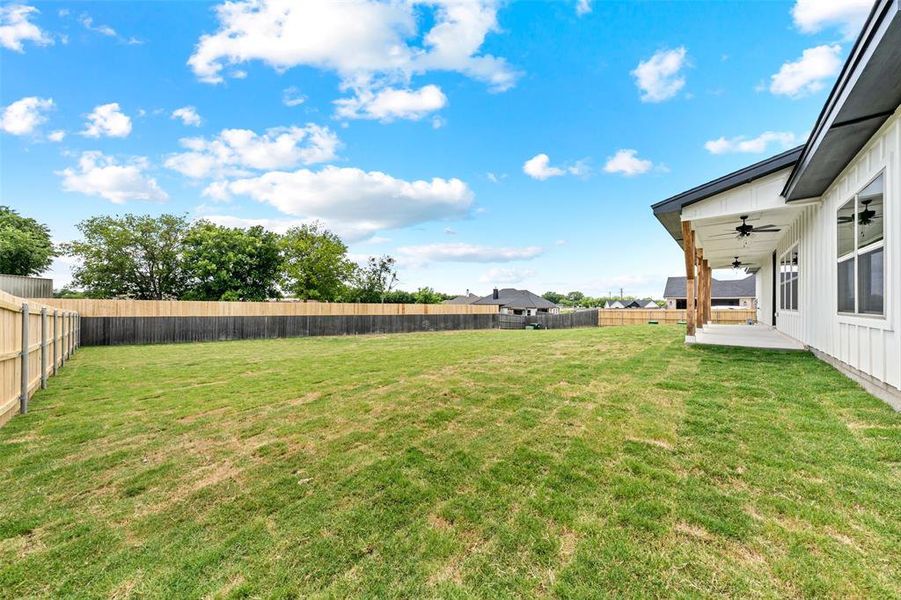 Spacious backyard featuring a wood privacy fence, expansive lawn, covered patio, wood-wrapped structural columns, and two ceiling fans Spacious backyard featuring a wood privacy fence, expansive lawn, covered patio, wood-wrapped structural columns, and two ceiling fans