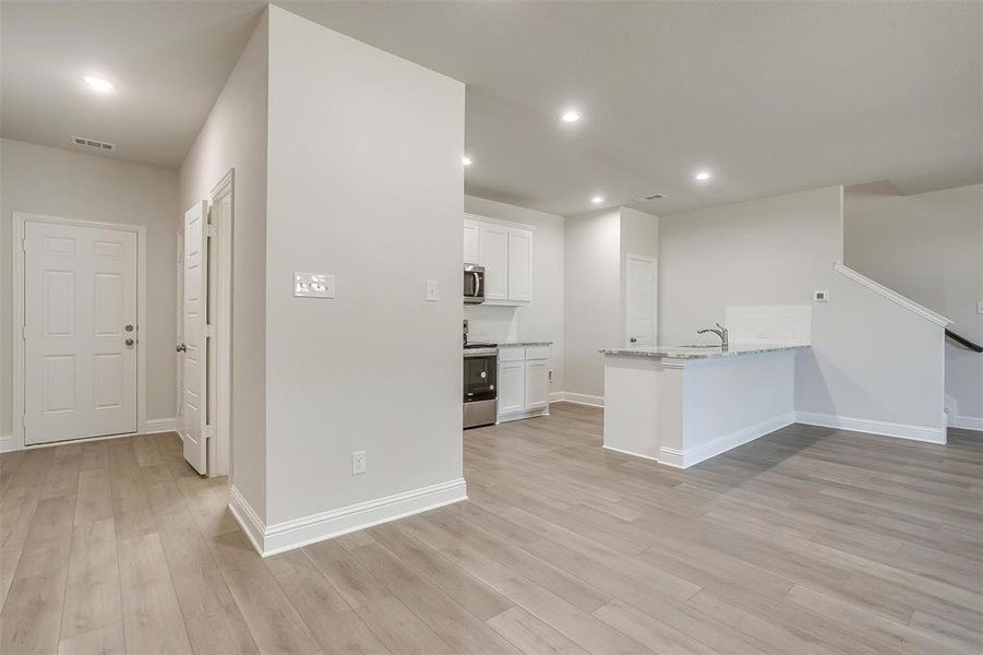 Kitchen featuring a peninsula, light stone counters, white cabinets, light wood-style flooring, and recessed lighting Kitchen featuring a peninsula, light stone counters, white cabinets, light wood-style flooring, and recessed lighting