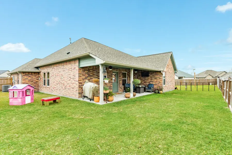 This photo showcases a brick home with a well-maintained backyard. It features a covered patio with seating and potted plants, ideal for outdoor relaxation. The yard is spacious and fenced, offering privacy and room for activities. With a touch of charm.