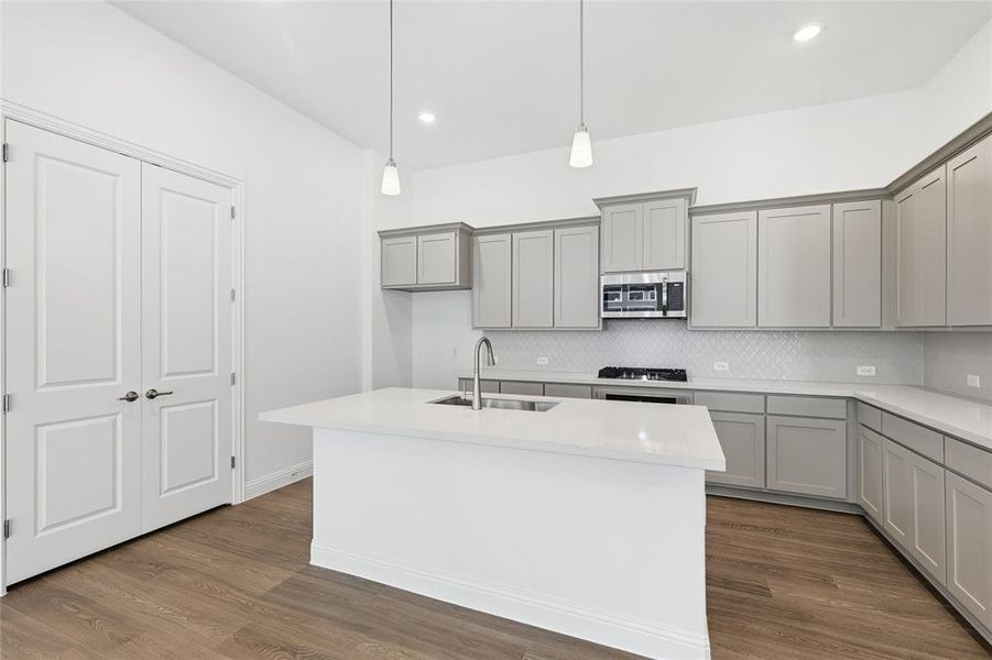 Kitchen featuring gray cabinets, a center island with sink, decorative backsplash, dark wood finished floors, and recessed lighting