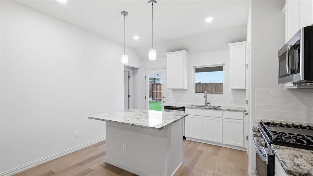 Modern kitchen featuring a central island with a granite countertop, white cabinetry, stainless steel appliances, and wood-finish flooring