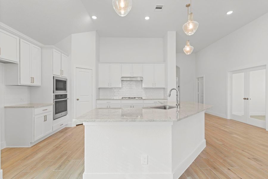 Wow what a home! Step into this stunning gourmet kitchen featuring bright white shaker cabinets, a large island with seating, pendant lighting, and beautiful wood-look tile floors. The open layout flows perfectly into the dining and family areas, ideal for cooking, gathering, and everyday living!