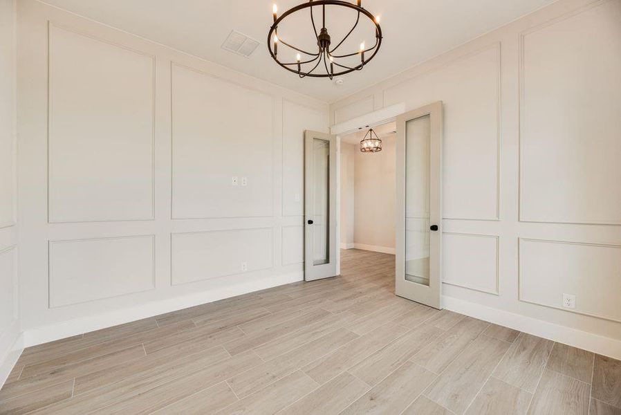 Spare room with a chandelier, a decorative wall, light wood-style flooring, and french doors Spare room with a chandelier, a decorative wall, light wood-style flooring, and french doors