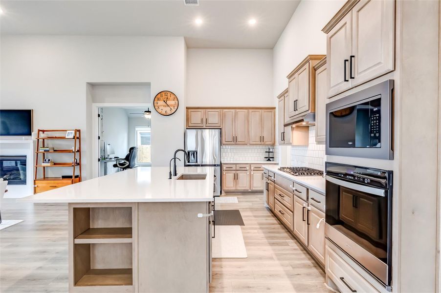 A well-appointed kitchen features stainless steel appliances, abundant cabinetry, and a large island, flowing into an open-concept living area.