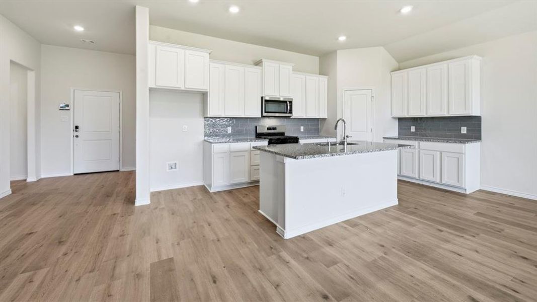 Kitchen with white cabinets, dark stone counters, stainless steel appliances, an island with sink, and light wood-style flooring