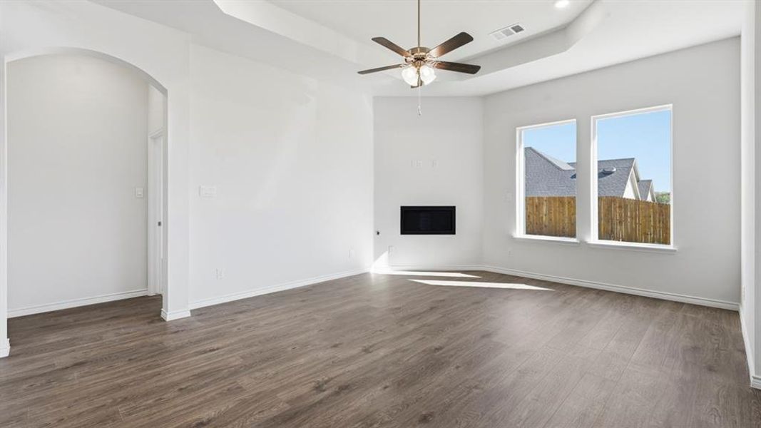 Unfurnished living room featuring a raised ceiling, a fireplace, dark wood-type flooring, a ceiling fan, and arched walkways Unfurnished living room featuring a raised ceiling, a fireplace, dark wood-type flooring, a ceiling fan, and arched walkways