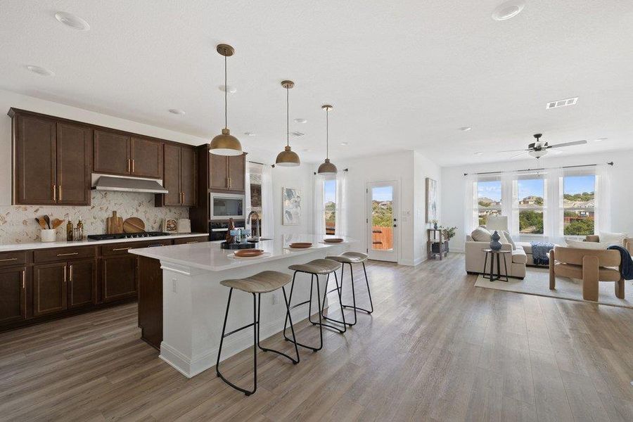 Kitchen with a kitchen bar, open floor plan, a kitchen island with sink, decorative light fixtures, and light wood-type flooring Kitchen with a kitchen bar, open floor plan, a kitchen island with sink, decorative light fixtures, and light wood-type flooring