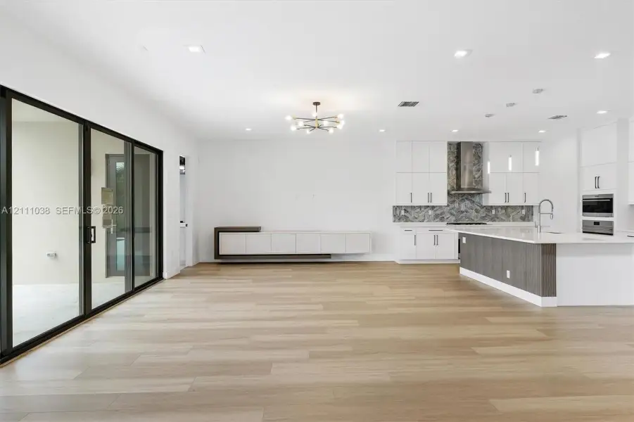 Open-concept living space featuring wood-finish flooring, a contemporary kitchen with built-in cabinetry, an island with stone-finish countertops, and large multi-panel sliding glass doors