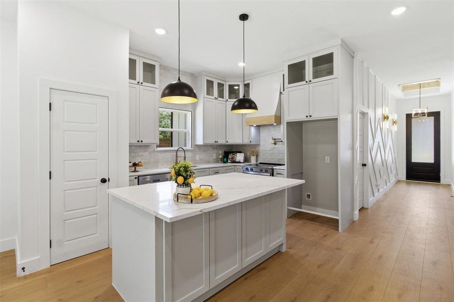 Kitchen featuring a central island with a light-toned countertop, white cabinetry with glass upper doors, stainless steel appliances, and wood-finish flooring