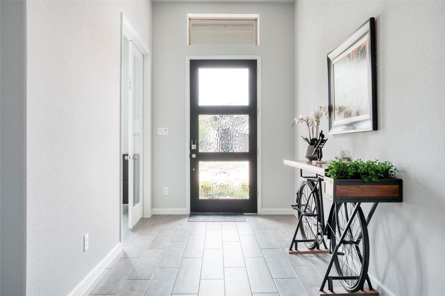 This photo showcases a bright and welcoming entryway with modern design elements. It features a glass-paneled front door, light-colored walls, and wood-look tile flooring. A unique console table doubles as a planter, adding a touch of greenery, and a large framed artwork adorns the wall. The space is both stylish and functional, offering a warm first impression. This photo showcases a bright and welcoming entryway with modern design elements. It features a glass-paneled front door, light-colored walls, and wood-look tile flooring. A unique console table doubles as a planter, adding a touch of greenery, and a large framed artwork adorns the wall. The space is both stylish and functional, offering a warm first impression.