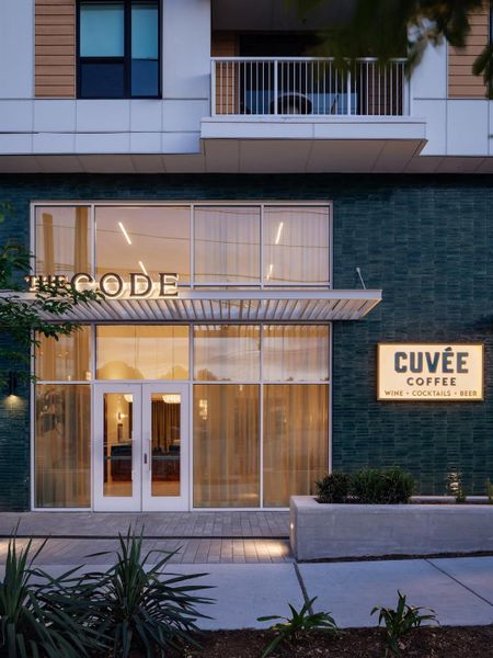 A modern mixed-use exterior displays a sleek glass storefront beneath structured residential balconies. A modern mixed-use exterior displays a sleek glass storefront beneath structured residential balconies.