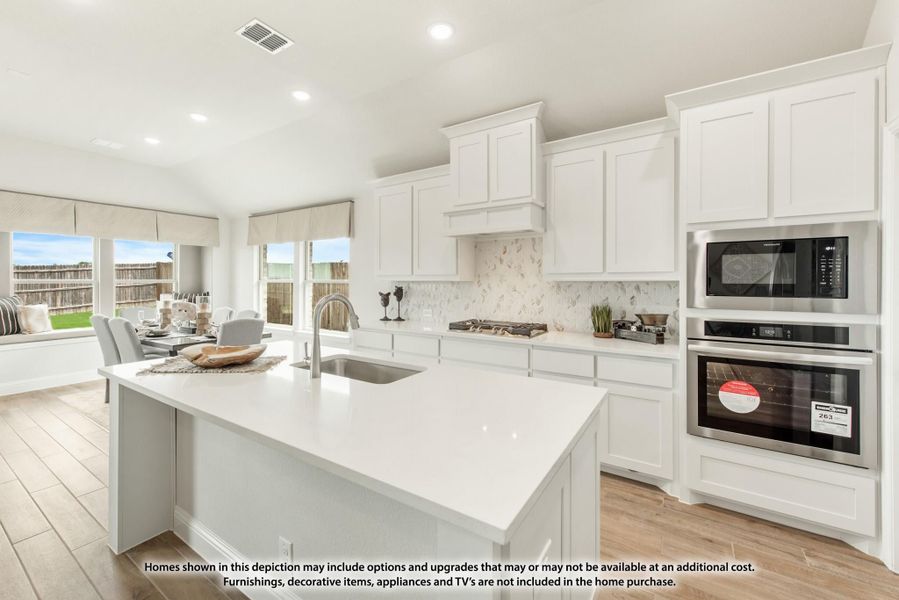 Kitchen with white cabinets, large island with sink, stainless steel wall oven and microwave, and marble tile backsplash.