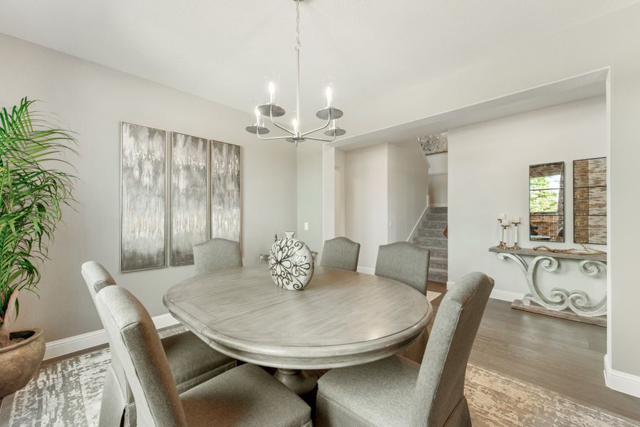 Dining room with round wood table, six gray upholstered chairs, and a chandelier overhead