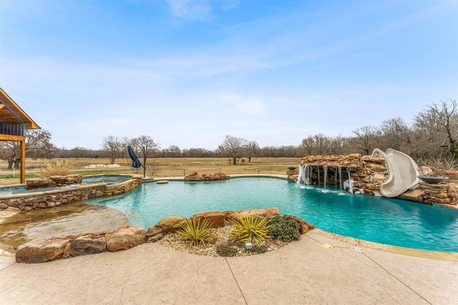 View of pool featuring a patio area, a water slide, and a pool with connected hot tub