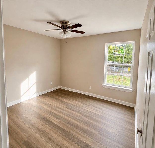 Neutral-toned room featuring wood-finish flooring, a ceiling fan with integrated lighting, and a double-hung window Neutral-toned room featuring wood-finish flooring, a ceiling fan with integrated lighting, and a double-hung window