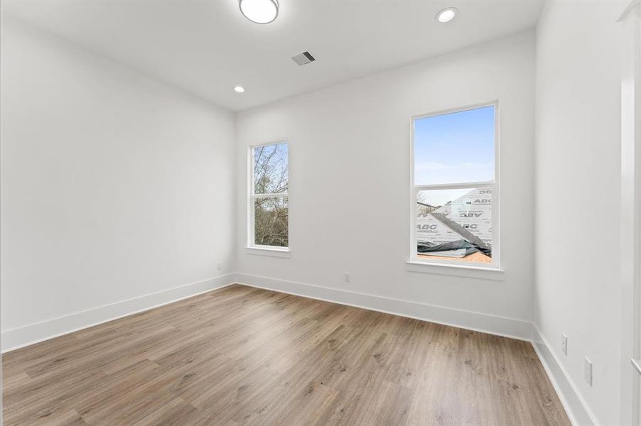 Bright, spacious room with natural light from two windows, light wood flooring, and recessed lighting. Perfect for a bedroom or office space.