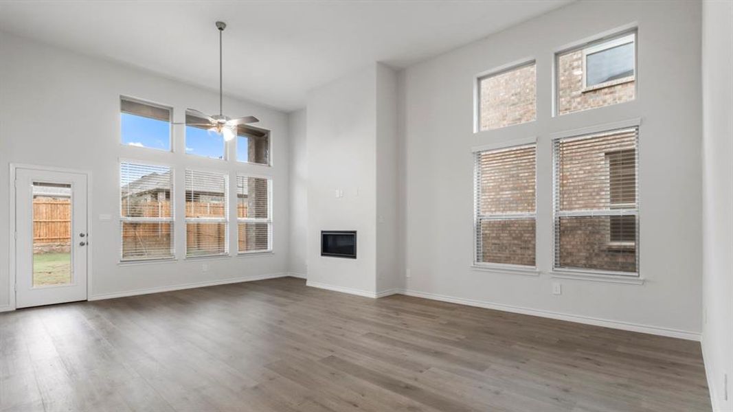Unfurnished living room featuring a high ceiling, wood finished floors, a glass covered fireplace, and ceiling fan Unfurnished living room featuring a high ceiling, wood finished floors, a glass covered fireplace, and ceiling fan