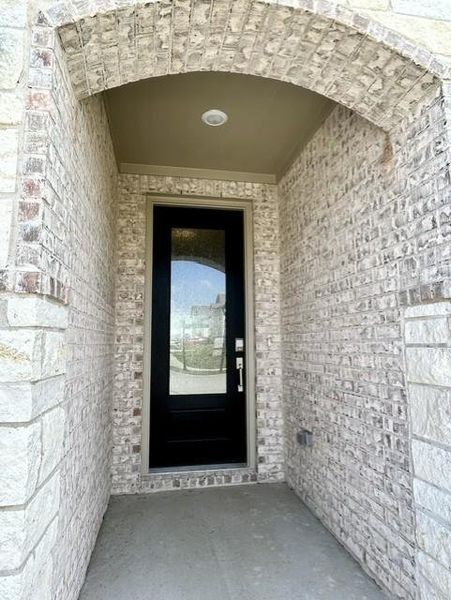 Entryway featuring a black paneled door with an integrated glass insert, set within an arched brick alcove Entryway featuring a black paneled door with an integrated glass insert, set within an arched brick alcove