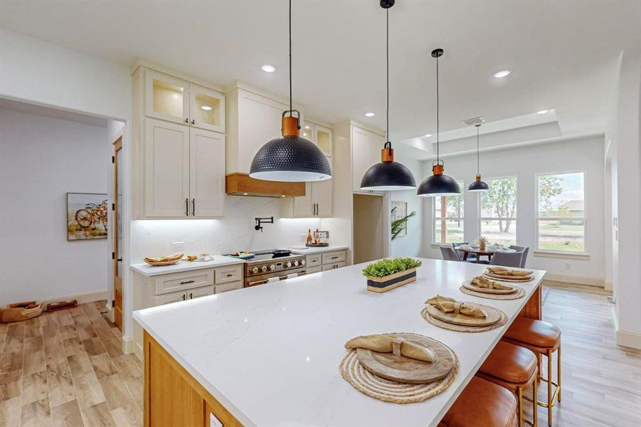 Kitchen featuring high end stainless steel range, pendant lighting, white cabinetry, light hardwood / wood-style flooring, and a kitchen island