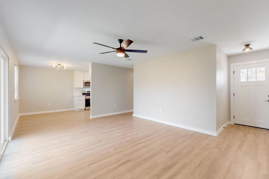 Unfurnished living room featuring visible vents, light wood-style flooring, ceiling fan, and baseboards