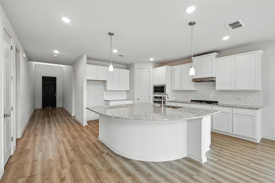Kitchen featuring backsplash, light stone countertops, white cabinets, light wood-style flooring, and recessed lighting Kitchen featuring backsplash, light stone countertops, white cabinets, light wood-style flooring, and recessed lighting