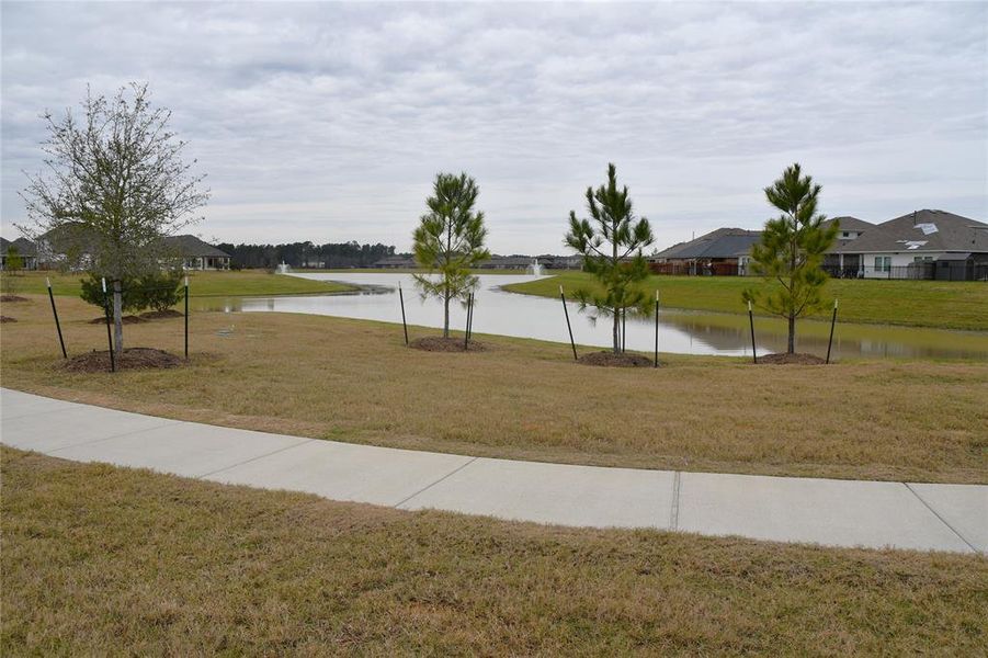 A serene neighborhood scene featuring a winding waterway and well-maintained grassy areas, with a paved walkway and surrounding homes. Ideal for tranquil living and scenic views.