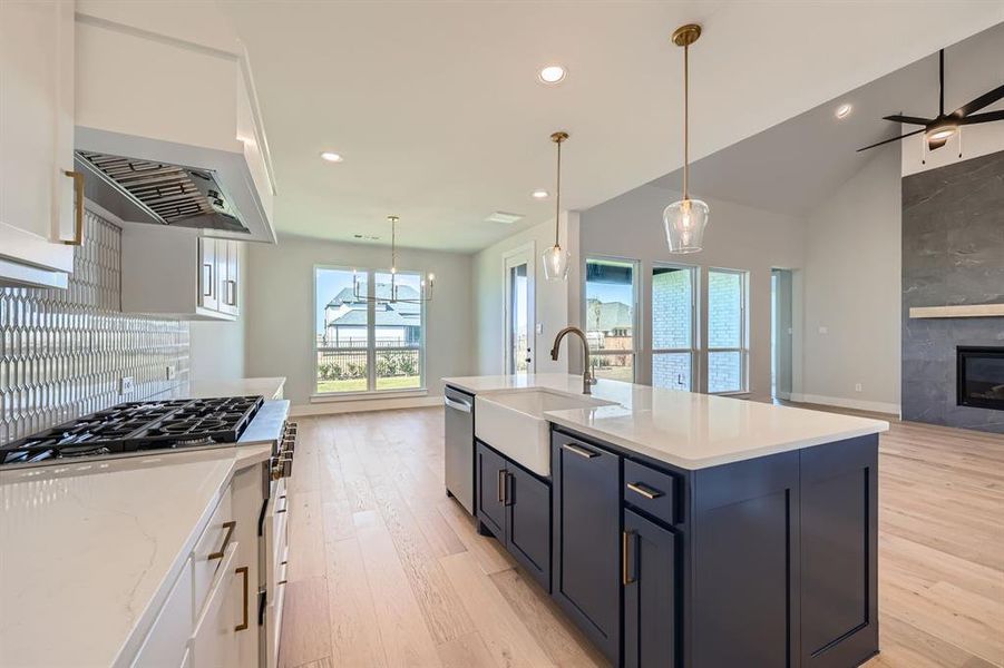 Kitchen with sink, a fireplace, white cabinets, a center island with sink, and light wood-type flooring