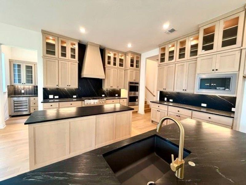 An inviting kitchen features a central island, rich dark countertops, and plentiful light-toned cabinetry. An inviting kitchen features a central island, rich dark countertops, and plentiful light-toned cabinetry.