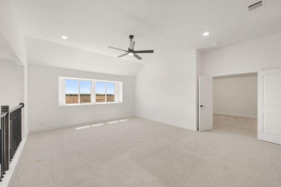 Spacious bonus room with vaulted ceiling, ceiling fan, carpet flooring, and large window with open field views