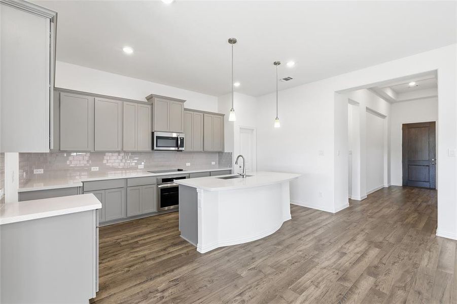 Modern kitchen featuring wood-finish flooring, light gray cabinetry, white countertops, a subway tile backsplash, and a curved island with pendant lighting