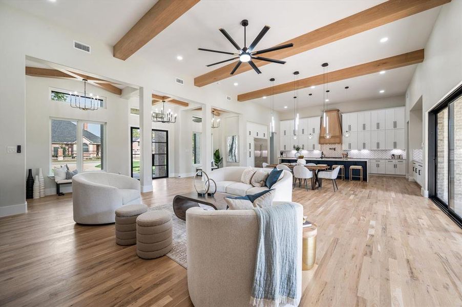 Living room featuring ceiling fan with notable chandelier, beamed ceiling, and light hardwood / wood-style floors