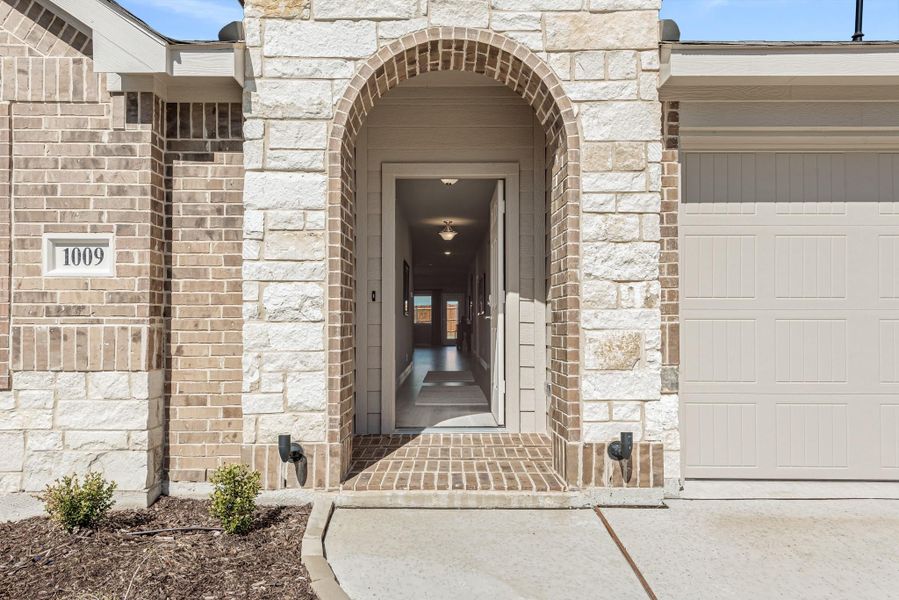 Home entrance with arched stone surround, brick exterior, open front door, and attached garage at address 1009. Home entrance with arched stone surround, brick exterior, open front door, and attached garage at address 1009.