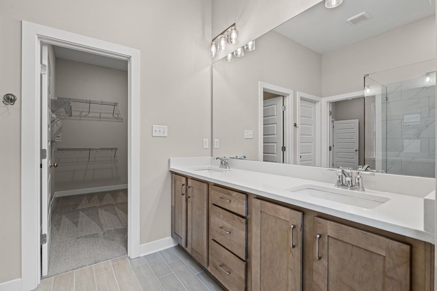 Full bath featuring double vanity, a walk in closet, light carpet, and tiled shower