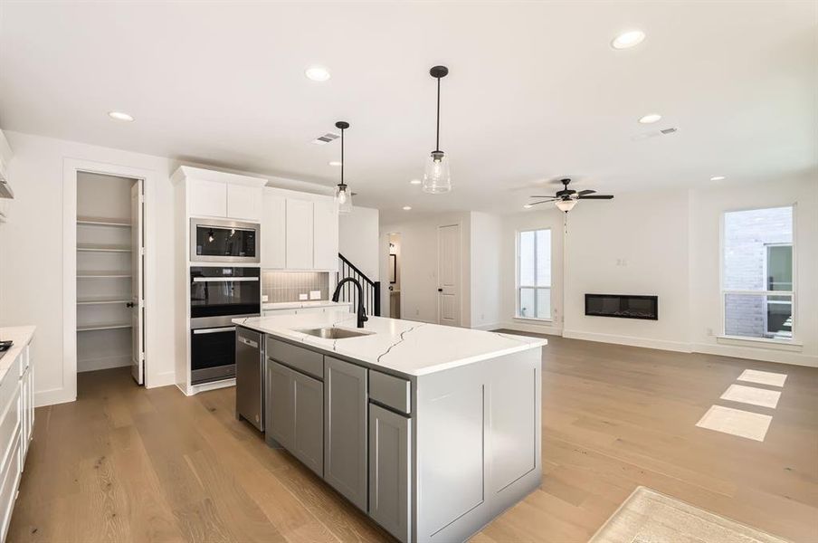 Kitchen with light hardwood / wood-style flooring, white cabinetry, sink, and a kitchen island with sink