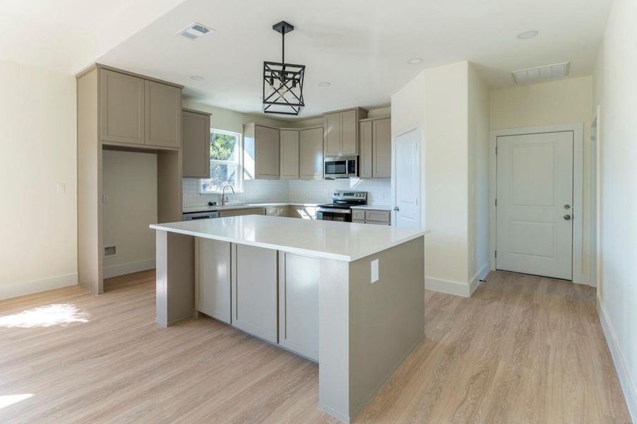Kitchen with gray cabinetry, backsplash, stainless steel appliances, a kitchen island, and recessed lighting