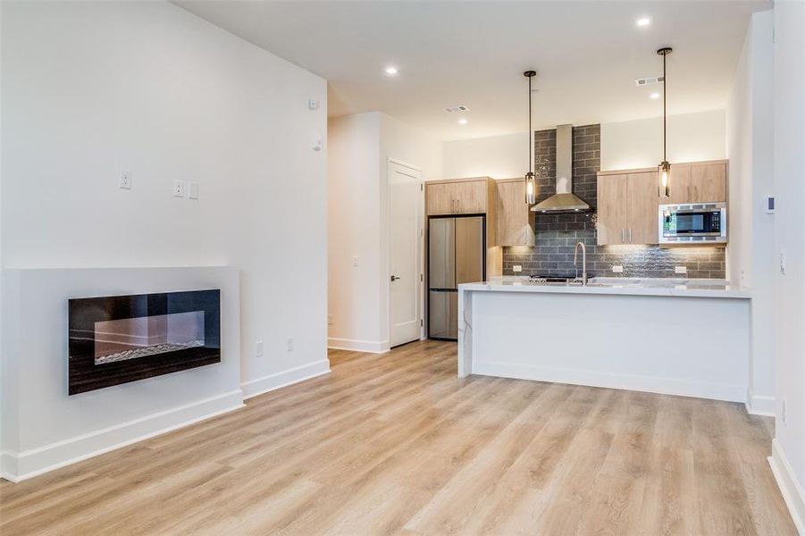 Kitchen featuring wall chimney range hood, light hardwood / wood-style flooring, tasteful backsplash, appliances with stainless steel finishes, and pendant lighting