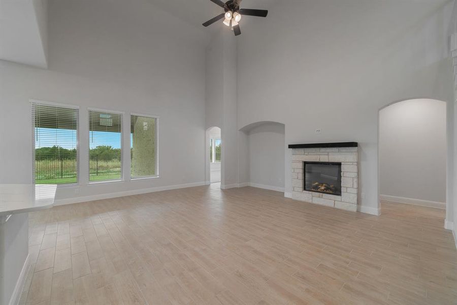 Unfurnished living room featuring a healthy amount of sunlight, light hardwood / wood-style flooring, ceiling fan, and a stone fireplace