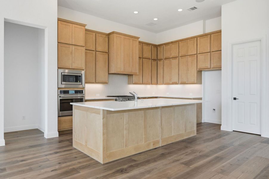 Kitchen featuring light brown cabinets, stainless steel appliances, light wood-style flooring, a center island with sink, and recessed lighting