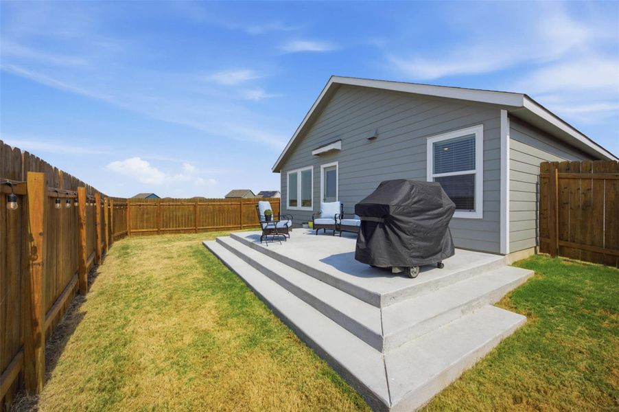 An elevated concrete patio overlooks a fenced backyard under open blue skies.