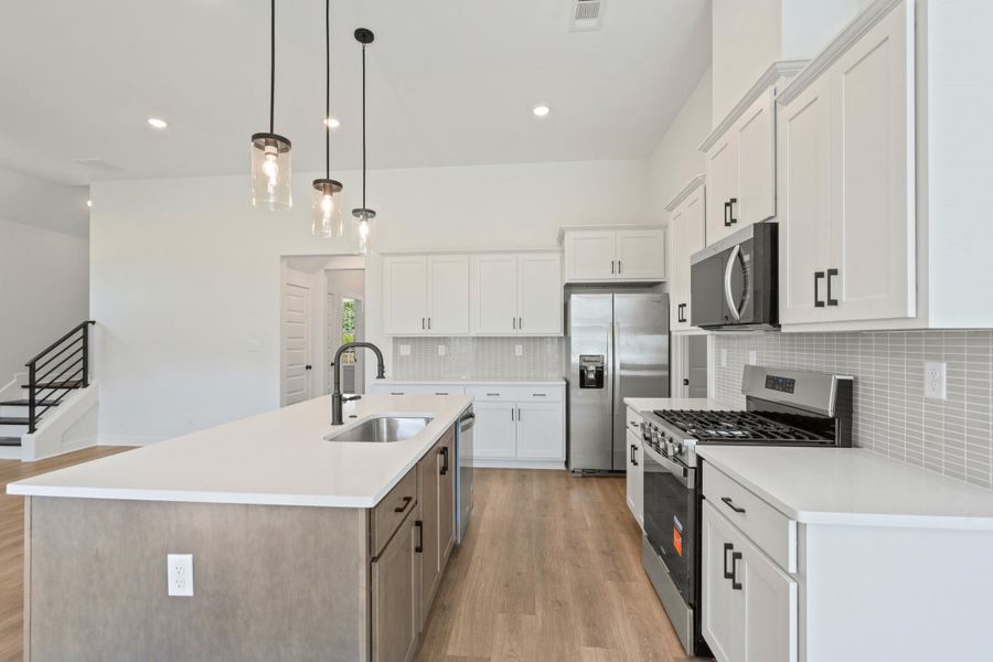 Kitchen featuring an expansive island with an undermount sink, pendant lighting, stainless steel appliances, and wood-finish flooring Kitchen featuring an expansive island with an undermount sink, pendant lighting, stainless steel appliances, and wood-finish flooring