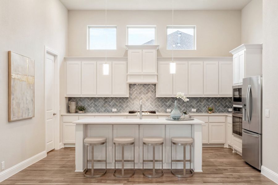 Kitchen with white cabinets, gray herringbone tile backsplash, center island with four barstools, and stainless steel appliances.