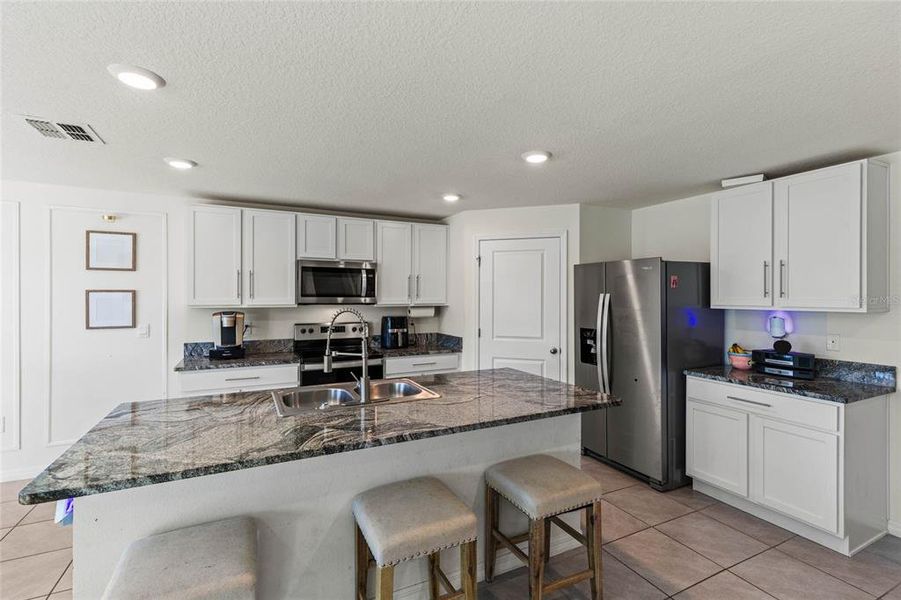 Kitchen showcasing white cabinets with granite countertops & stainless steel appliances